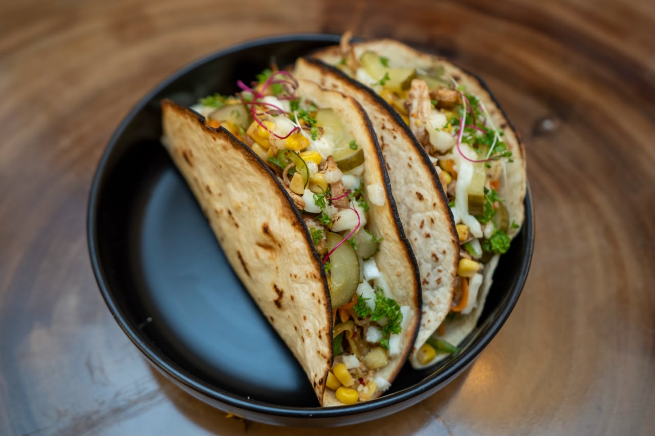 Two filled tacos on a dark plate
